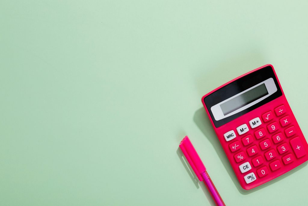 Pink calculator and pen on a pastel green background with copy space.